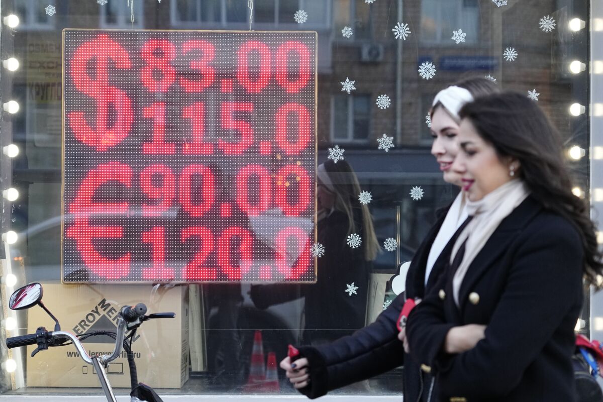 People walk past a currency exchange office screen displaying the exchange rates of U.S. Dollar and Euro to Russian Rubles in Moscow's downtown, Russia, Monday, Feb. 28, 2022. Moscow’s war on Ukraine and the ferocious financial backlash it’s unleashed are not only inflicting an economic catastrophe on President Vladimir Putin’s Russia. The repercussions are also menacing the global economy and shaking financial markets. (AP Photo/Pavel Golovkin)