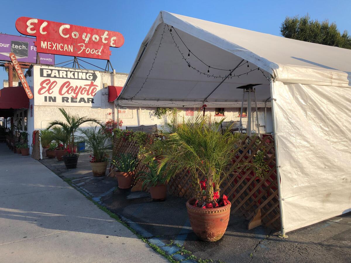 A white party tent is seen in the foreground of El Coyote's retro Modernist signage, which rises above their building.