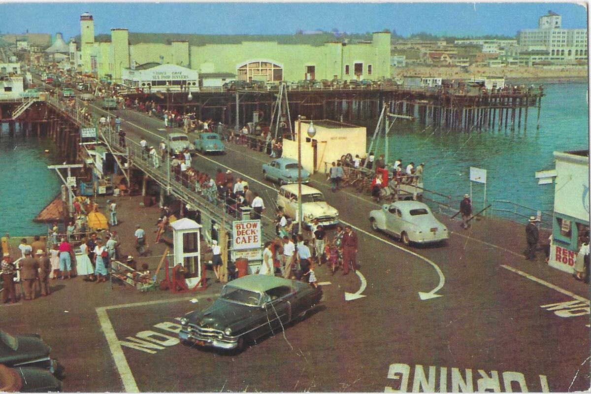 Cars and people on a pier, with a greenish building in the background.