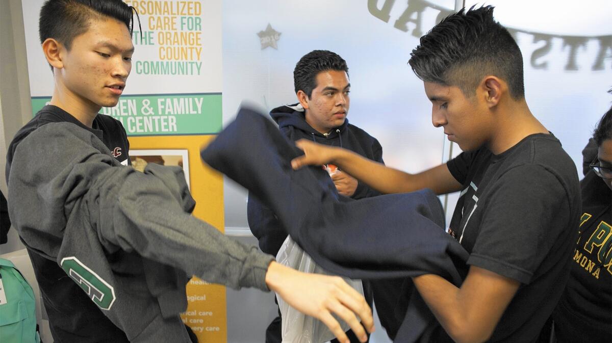 Costa Mesa High School seniors, from left, Duy Vu, Luis Ceja and Ricardo Resendiz put on their college sweatshirts during a Share Our Selves high school senior project ceremony. Vu will attend Golden West College. Ceja and Resendiz are headed to California State University, Fullerton.
