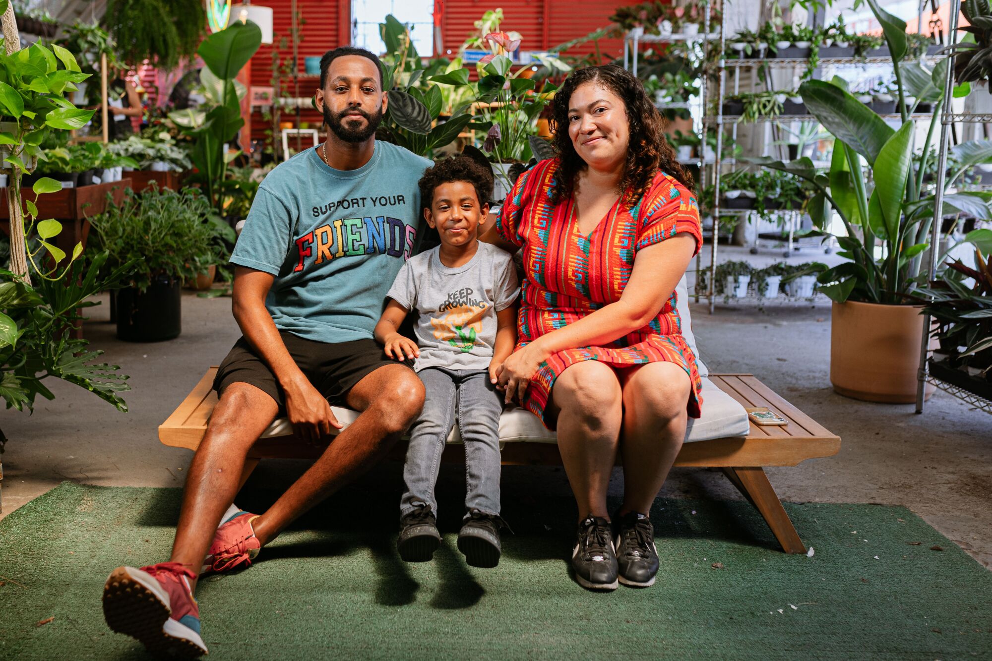 Parents sit on either side of their young son on a bench inside their auto shop turned plant shop.