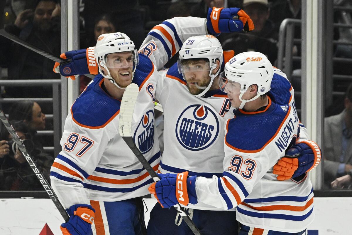 Three hockey players in blue, orange and white uniforms embrace on the ice.