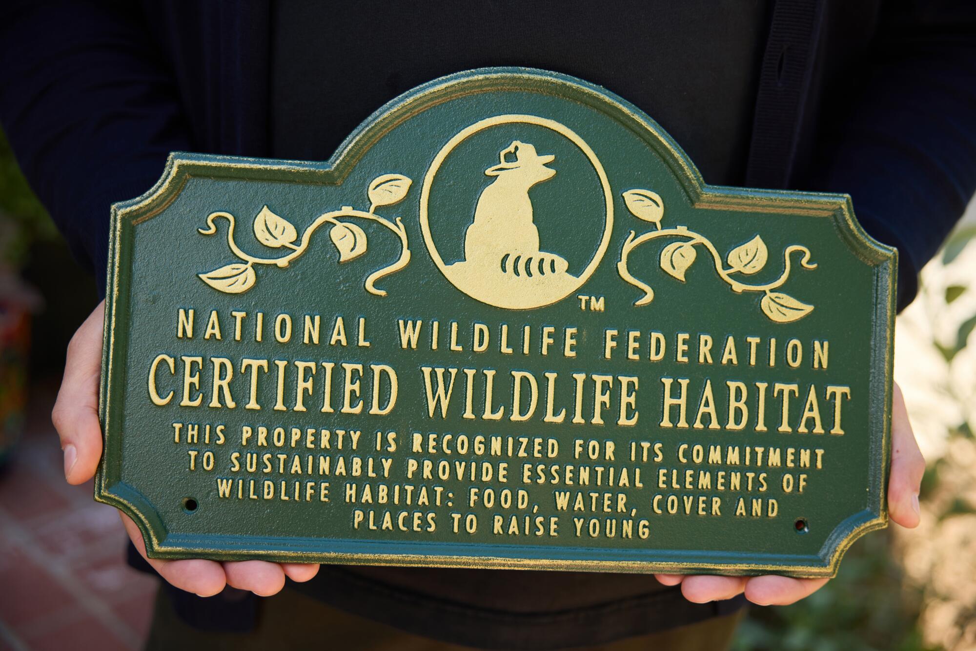 Two lands holding a green metal plaque reading "Certified Wildlife Habitat."