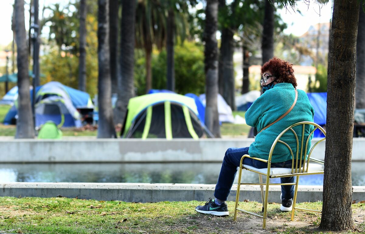 A woman sits in Echo Park as tents that are part of a large homeless encampment sit by the lake. 
