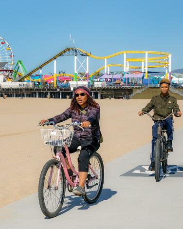SANTA MONICA, CA-APRIL 5, 2023: Damien Blackshaw, right, the founder of The Real Los Angeles Tours, rides along a bicycle path at Santa Monica State Beach with Meeka Smith, 43, and her son Gavin Long, 15, visiting from Baltimore, Maryland, while giving them a tour of Santa Monica and Venice. Blackshaw created a whole section on the company's website about tipping in the U.S. (Mel Melcon / Los Angeles Times)
