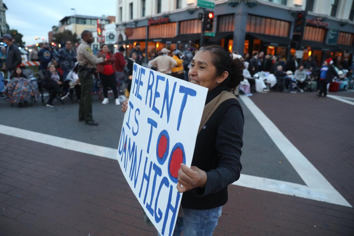 A protestor holds a sign that says "The rent is too damn high"