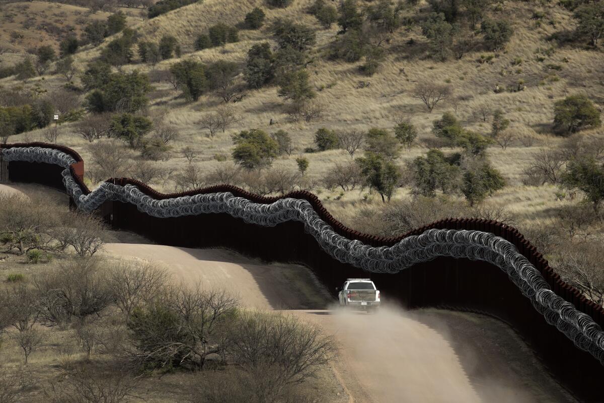 A Customs and Border Protection agent patrolling the U.S. side of a razor-wire-covered border wall east of Nogales, Ariz.