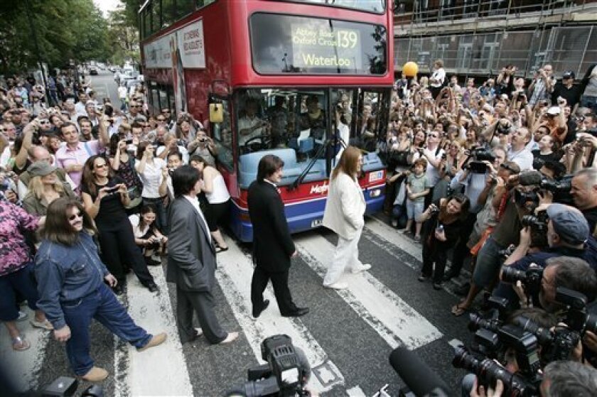 A tribute band dressed as members of British band, the Beatles, walk across the famous pedestrian crossing on Abbey Road