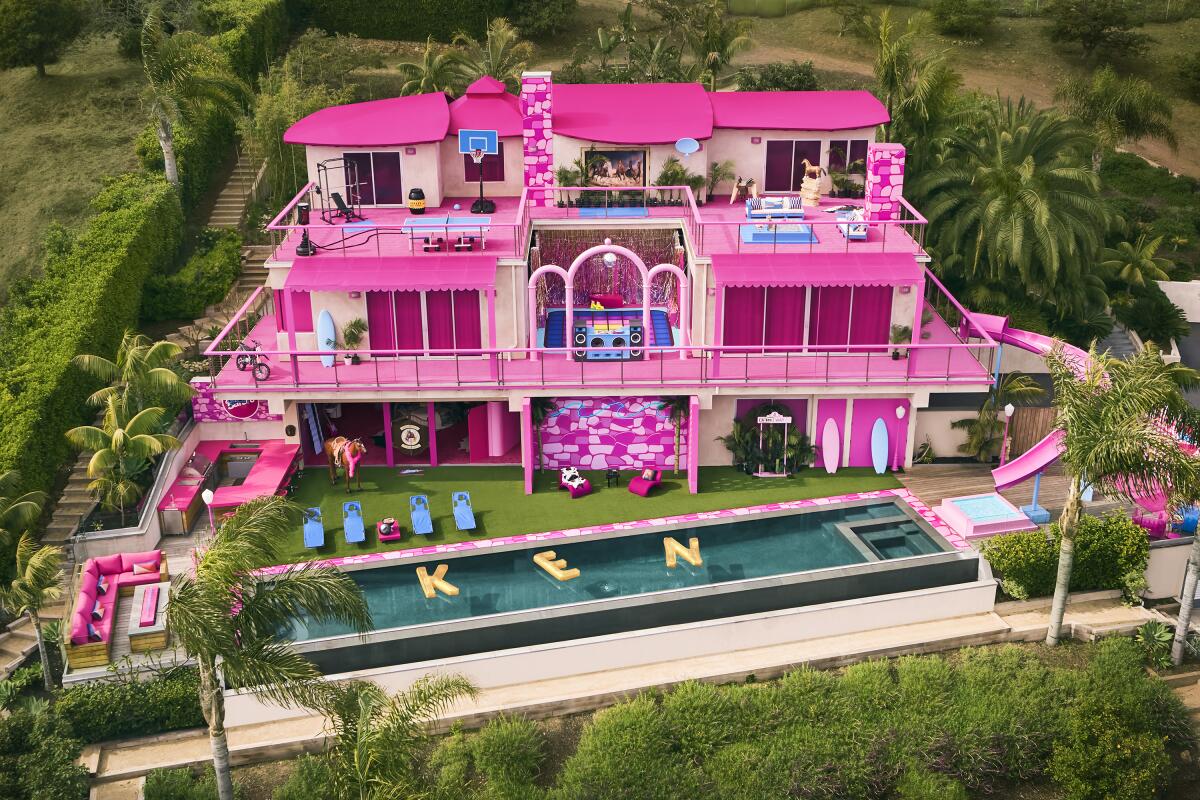 A giant pink mansion with a pool and waterslide surrounded by lots of plant life.