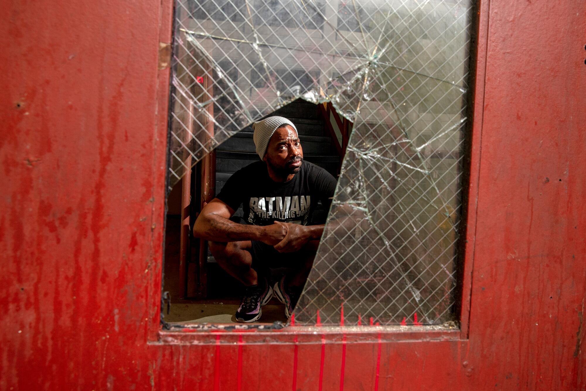 A man looks through a broken glass panel of an exit door