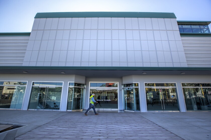 A worker in a hard hat and high-visibility vest walks past glass doors of an empty building