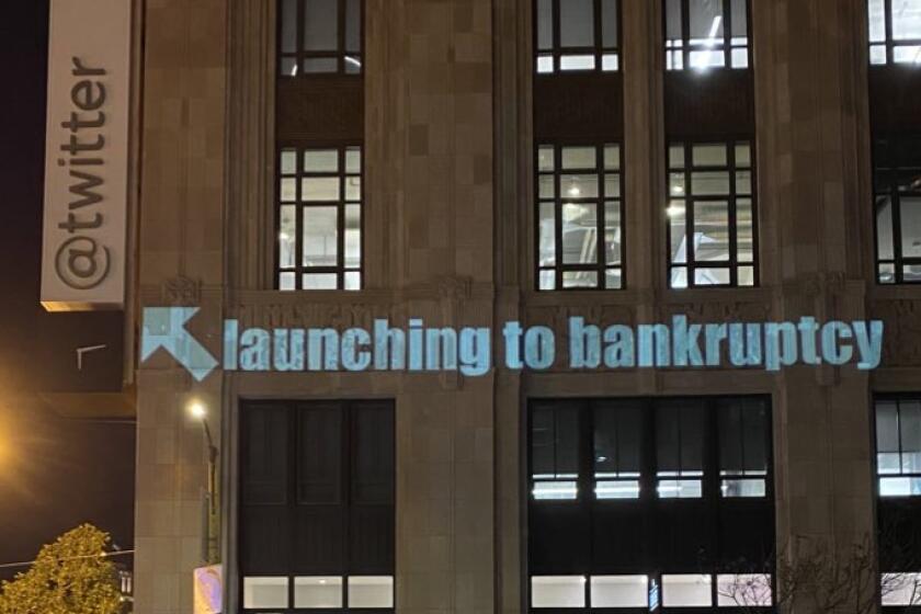 Large office building at night with "Launching to bankruptcy" projected on the front, pointing to a Twitter logo