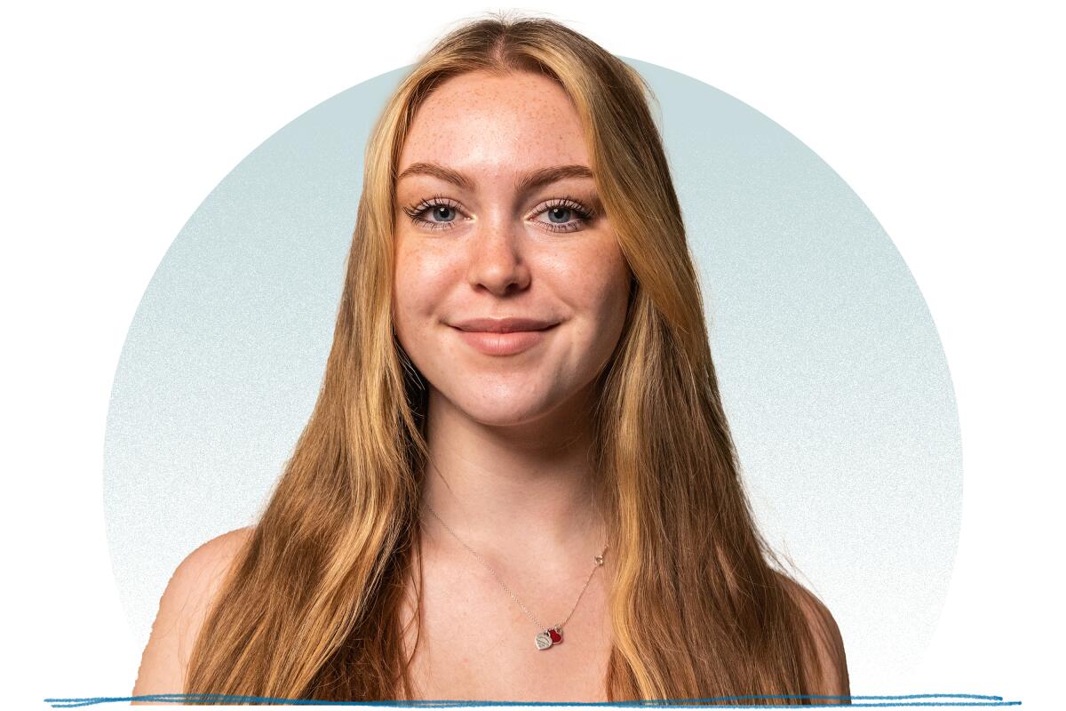 A young woman with long blonde hair and a gold necklace smiling for a portrait.