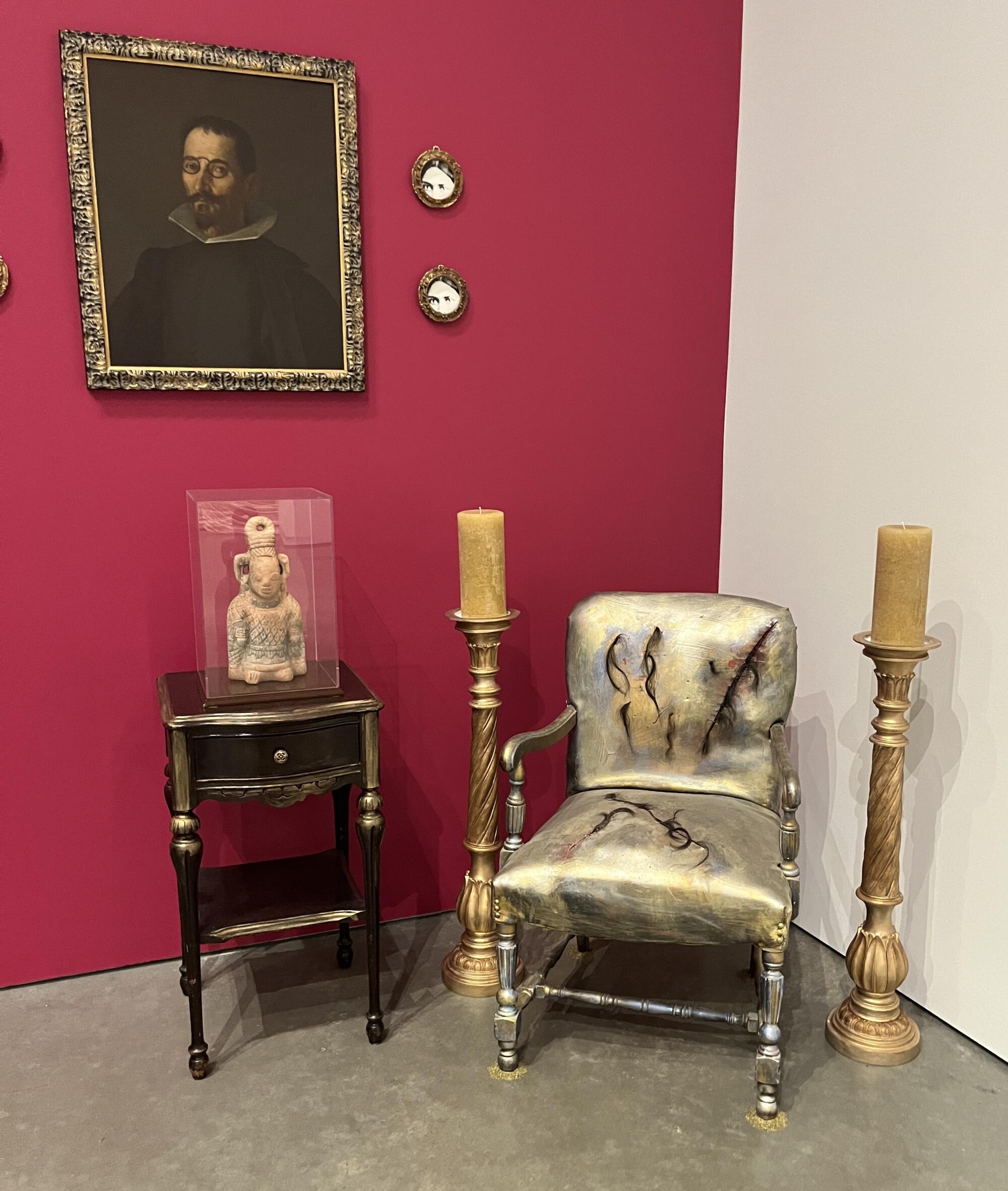 A small table bears a pre-Columbian figurine next to a chair painted gold and a pair of candelabra.