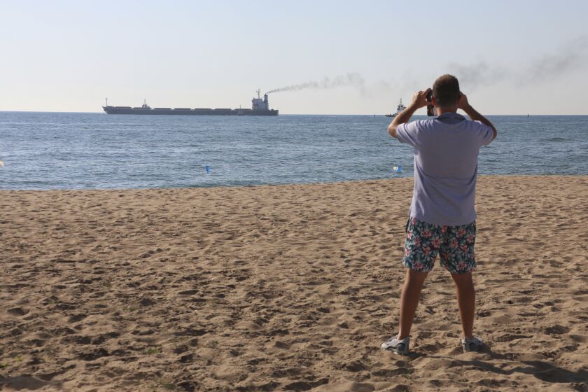 A man takes a picture as the Glory bulk carrier makes its way from the port in Odesa, Ukraine, Sunday, Aug. 7, 2022. According to Ukraine's Ministry of Infrastructure, the ship under the Marshall Islands' flag is carrying 66 thousand tons of Ukrainian corn. (AP Photo/Nina Lyashonok)