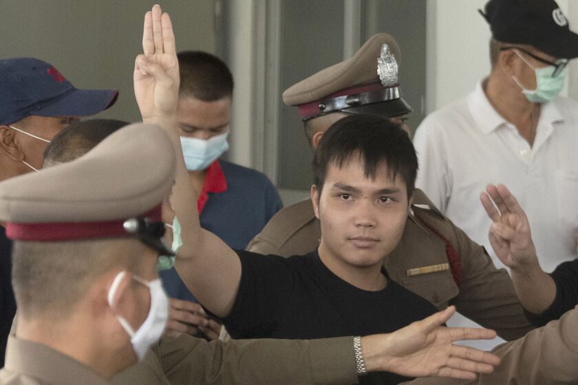 Tattep Ruangprapaikitseree raises a three-finger salute, a symbol of resistance, as he leaves the Samranrat police station.