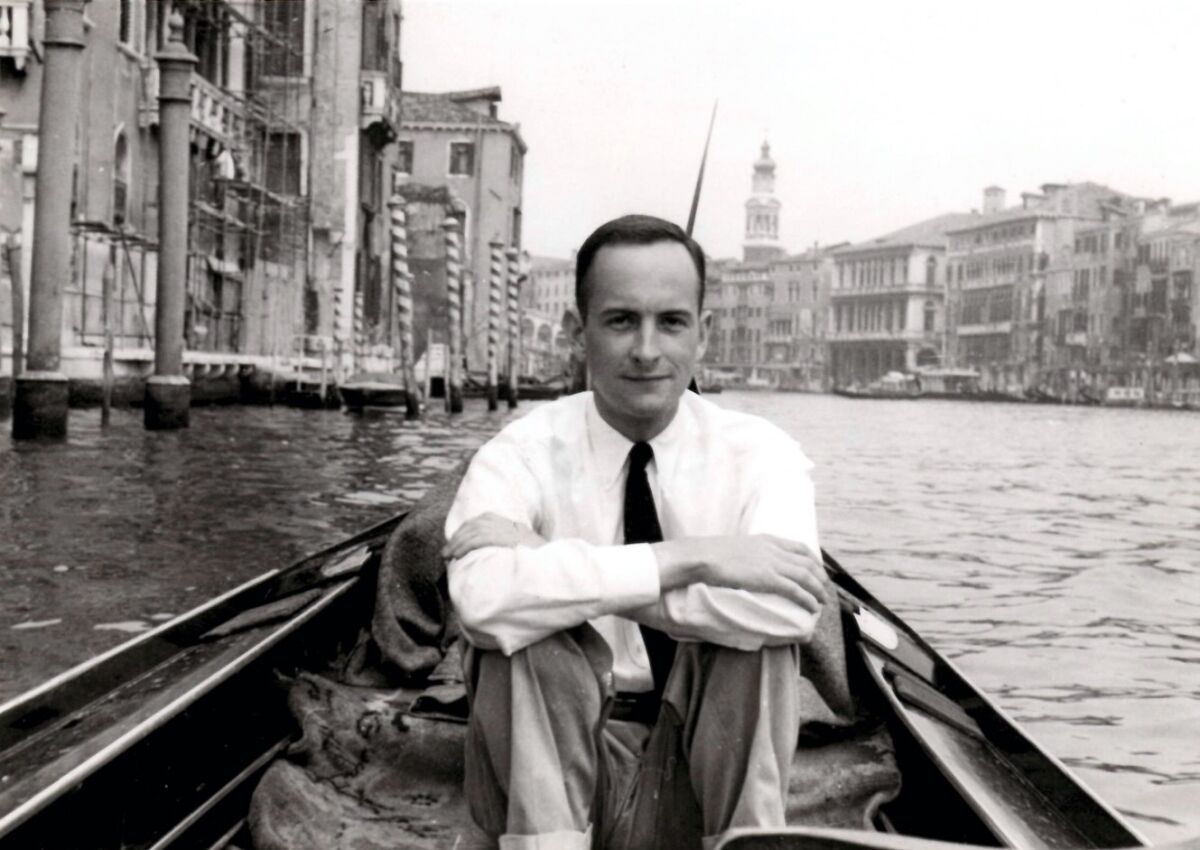 A man wearing a shirt and tie sits in a boat in Venice's Grand Canal