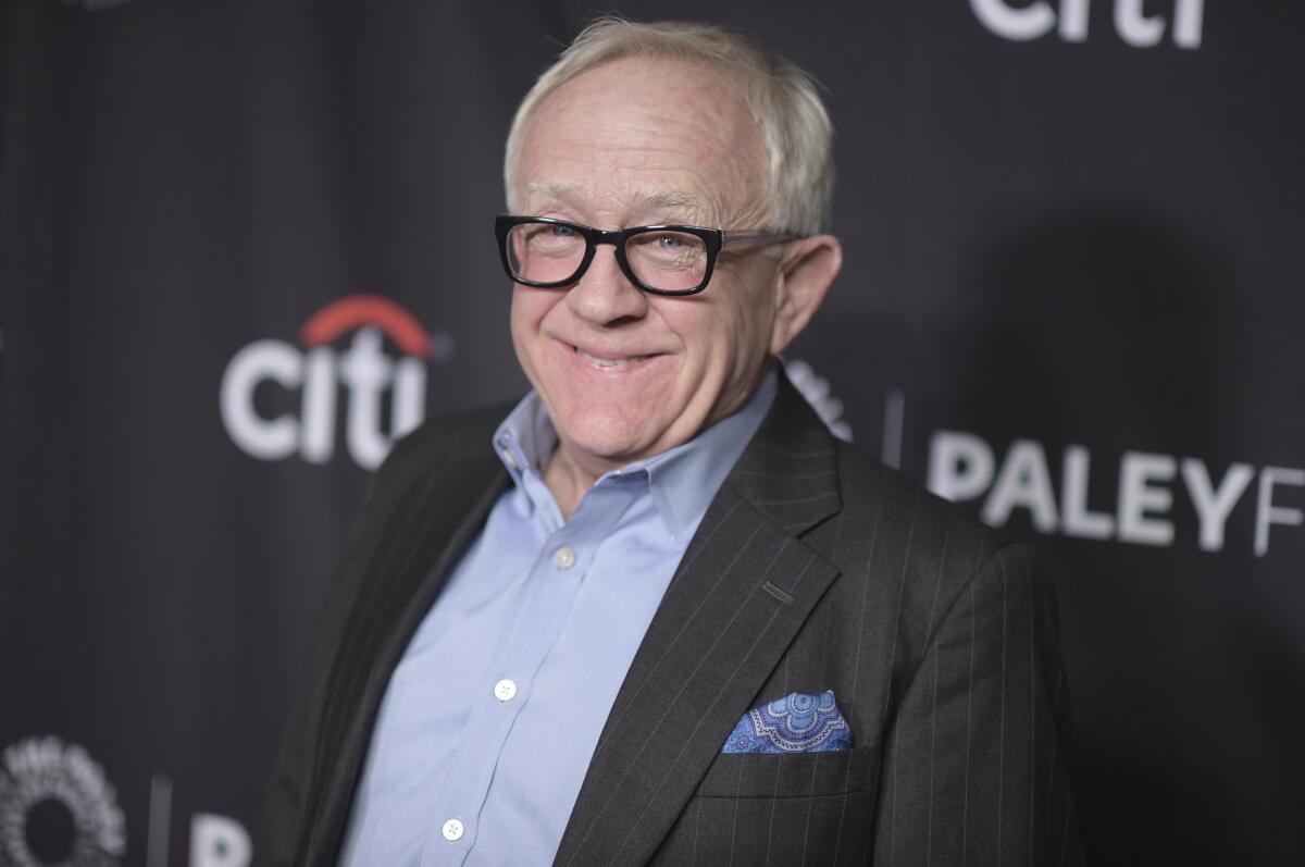 A man with white hair and black glasses smiling and wearing a suit