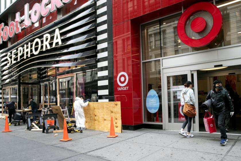 FILE - In this Friday, March 20, 2020 file photo, a shopper leaves the Target Store on 34th St. with supplies as carpenter board up the Sephora story in New York. Target Corp. said Friday it will give a $2 an hour wage increase to its 300,000-plus workers who have been scrambling to help customers. The pay bump will be effective at least through May 2. (AP Photo/Mary Altaffer, File)