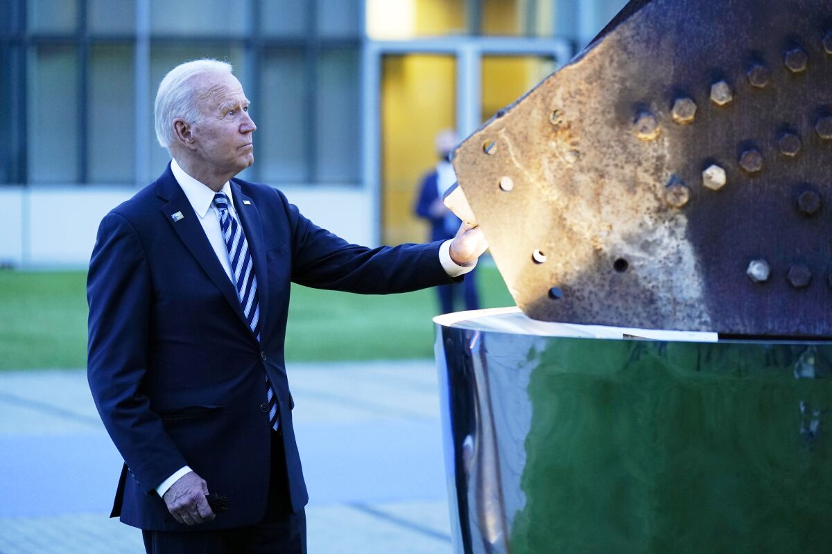 A man in a blue suit and striped tie touches a large steel sculpture on the right