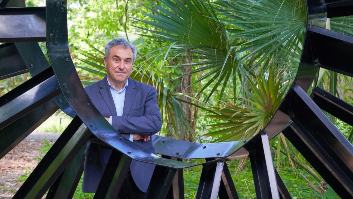 Palm Springs Art Museum Director Louis Grachos in front of foliage outdoors while looking through a metal structure