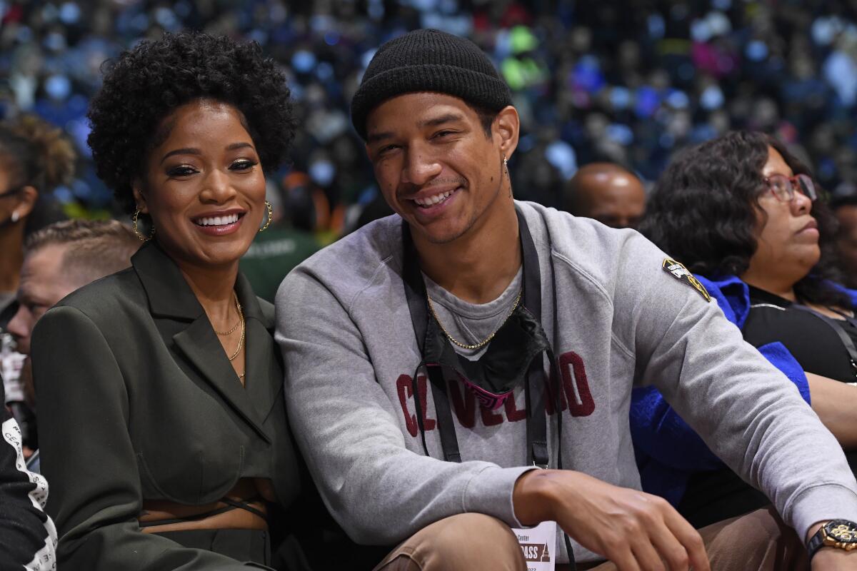 Keke Palmer wears a gray suit and smiles as she sits next to Darius Jackson who is wearing a gray long-sleeve shirt