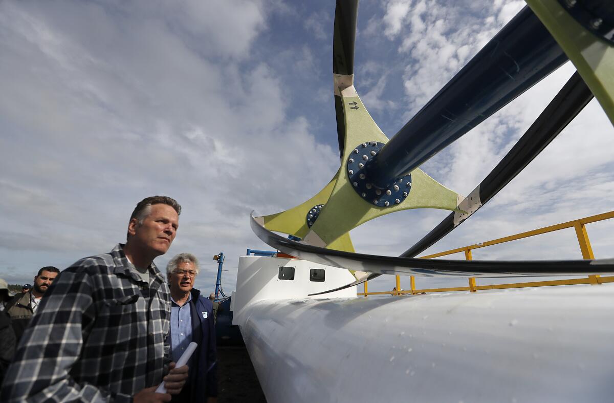 Alaska Gov. Mike Dunleavy looks at a hydroelectricity generator in Igiugig, a village in the state's southwest region. Residents of Igiugig and other remote areas are struggling with the effects of state government budget cuts from Dunleavy's line-item vetoes.