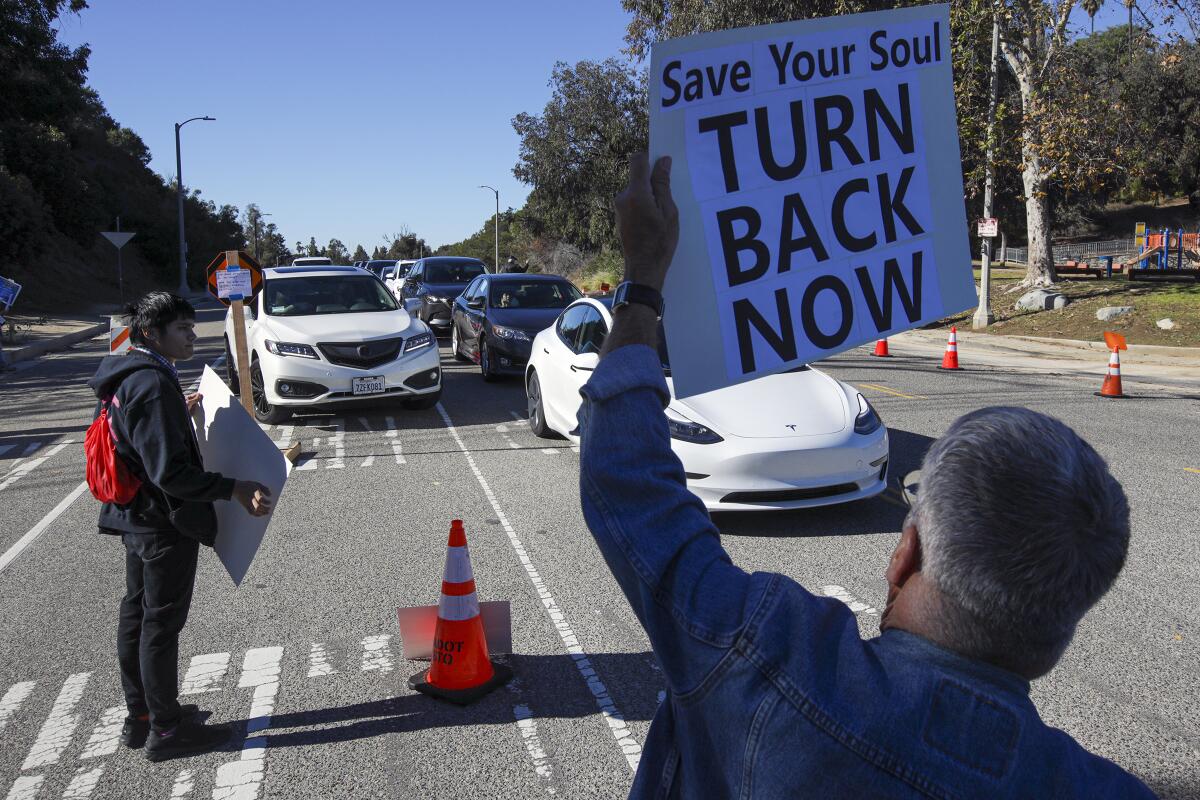Protesters with signs, one that reads Save your soul, turn back now, stand in front of a line of cars