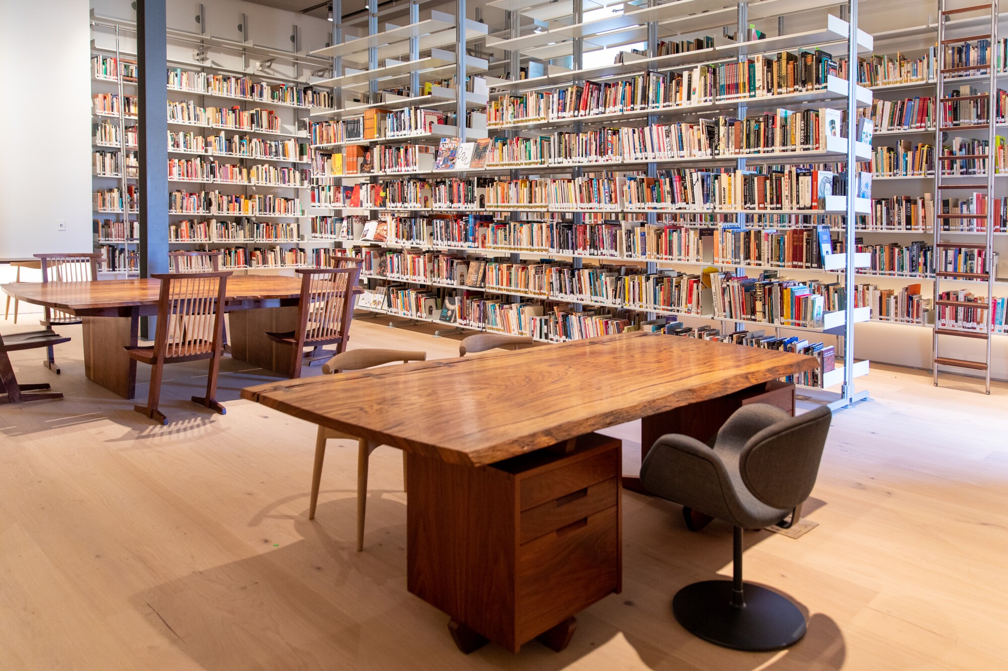 Two hand-crafted wood desks by George Nakashima are seen against a backdrop of Vitsoe 606 book shelves.