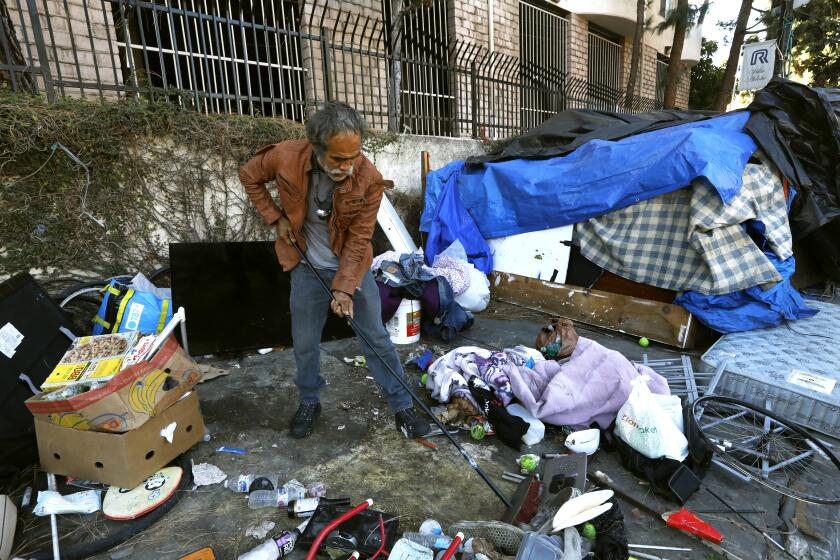 Los Angeles, California-Oct. 12, 2021-A man living on W. 4th Street tries to clear the sidewalk before city sanitation workers cleaned the whole street in Los Angeles on Oct. 12, 2021. (Carolyn Cole / Los Angeles Times)