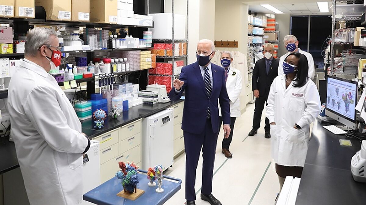 President Biden, in a dark suit and striped tie, talks with scientists.