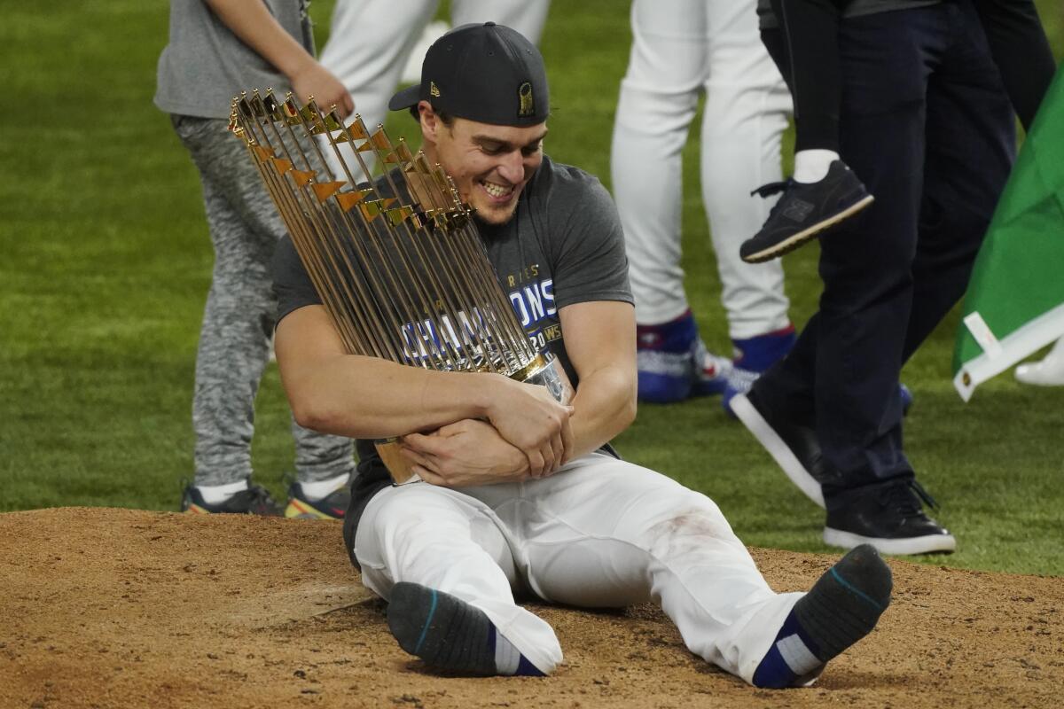Kiké Hernández sits on the field with legs outstretched, holding the World Series trophy.