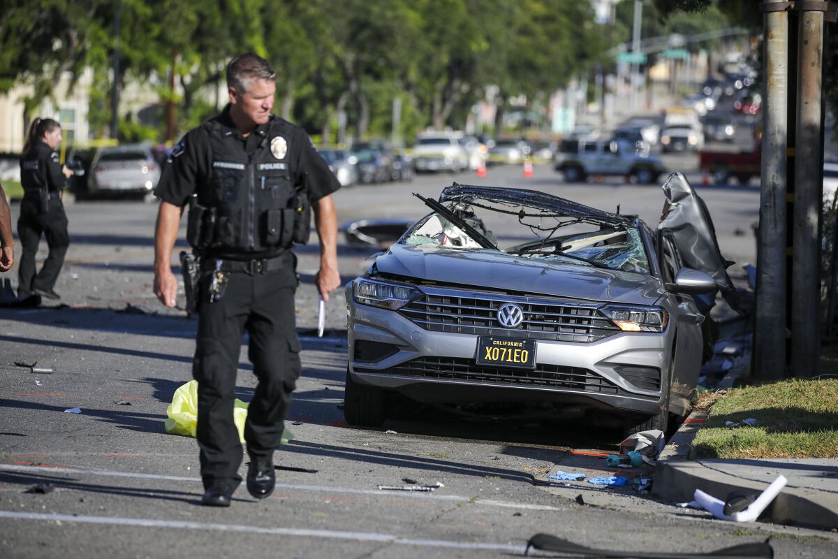 A police officer walks near a smashed car on a city street.