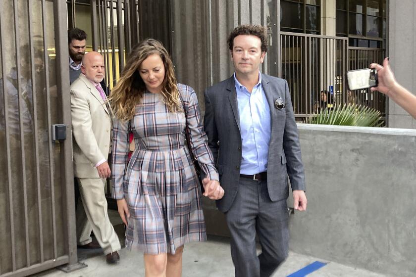 Danny Masterson wearing a suit is holding hands with Bijou Phillips who is wearing a plaid dress outside a courthouse