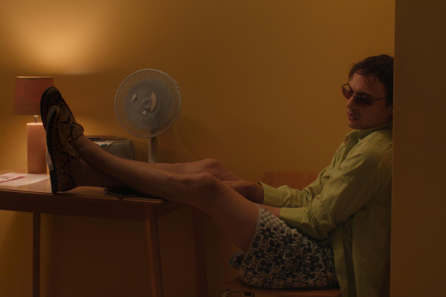 A man in shades puts his feet up on a desk.