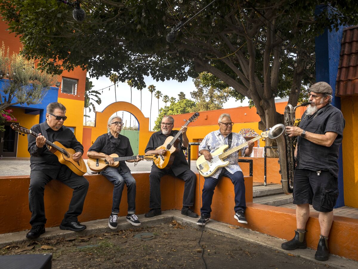 Five members of the band Los Lobos hold musical instruments.