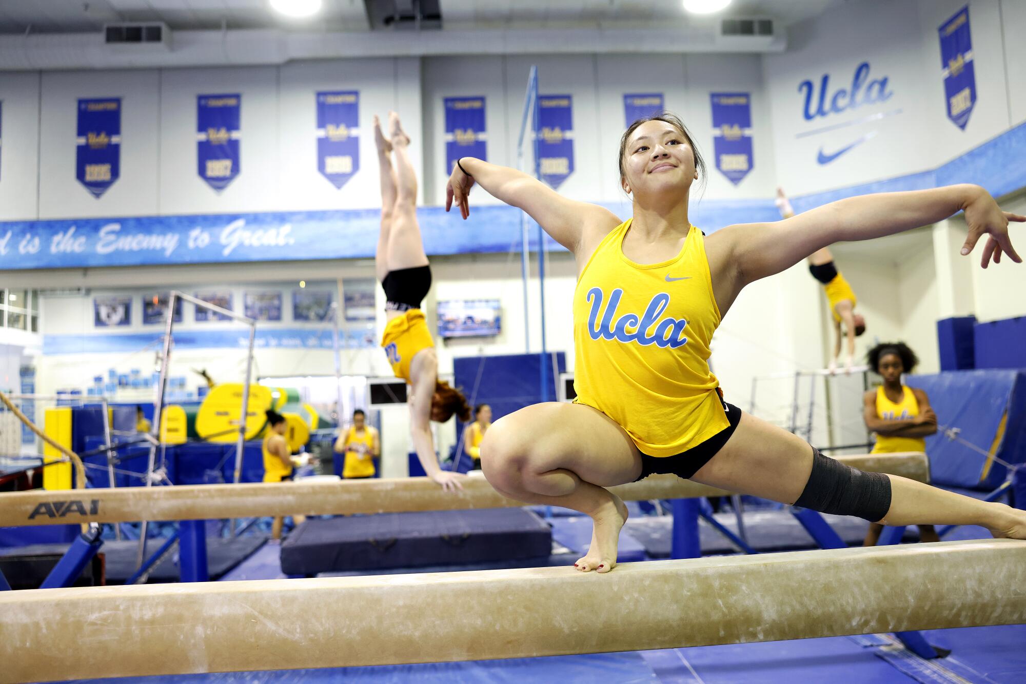 Emma Malabuyo smiles while extending her arms and working out on the beam.