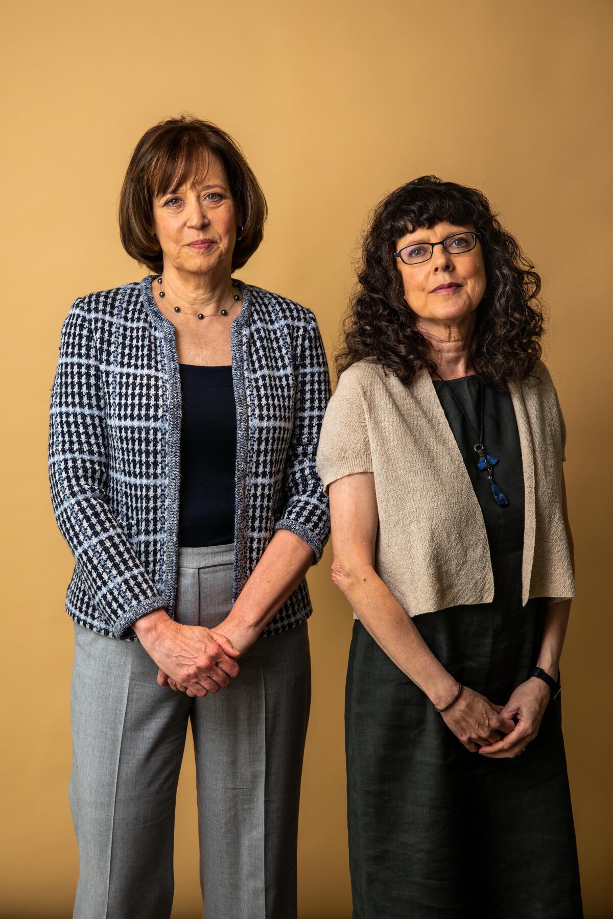 Two women pose for a portrait against a gold background. 