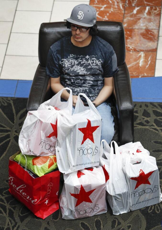 Robert Villalpando, 19, guards bags of purchased items while other members of his family shop for more during Black Friday shopping at the Westfield Plaza Bonita mall in National City.