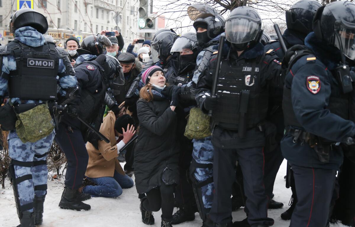 Police detain a man, on his knees amid snow, as another officer stops a young woman.