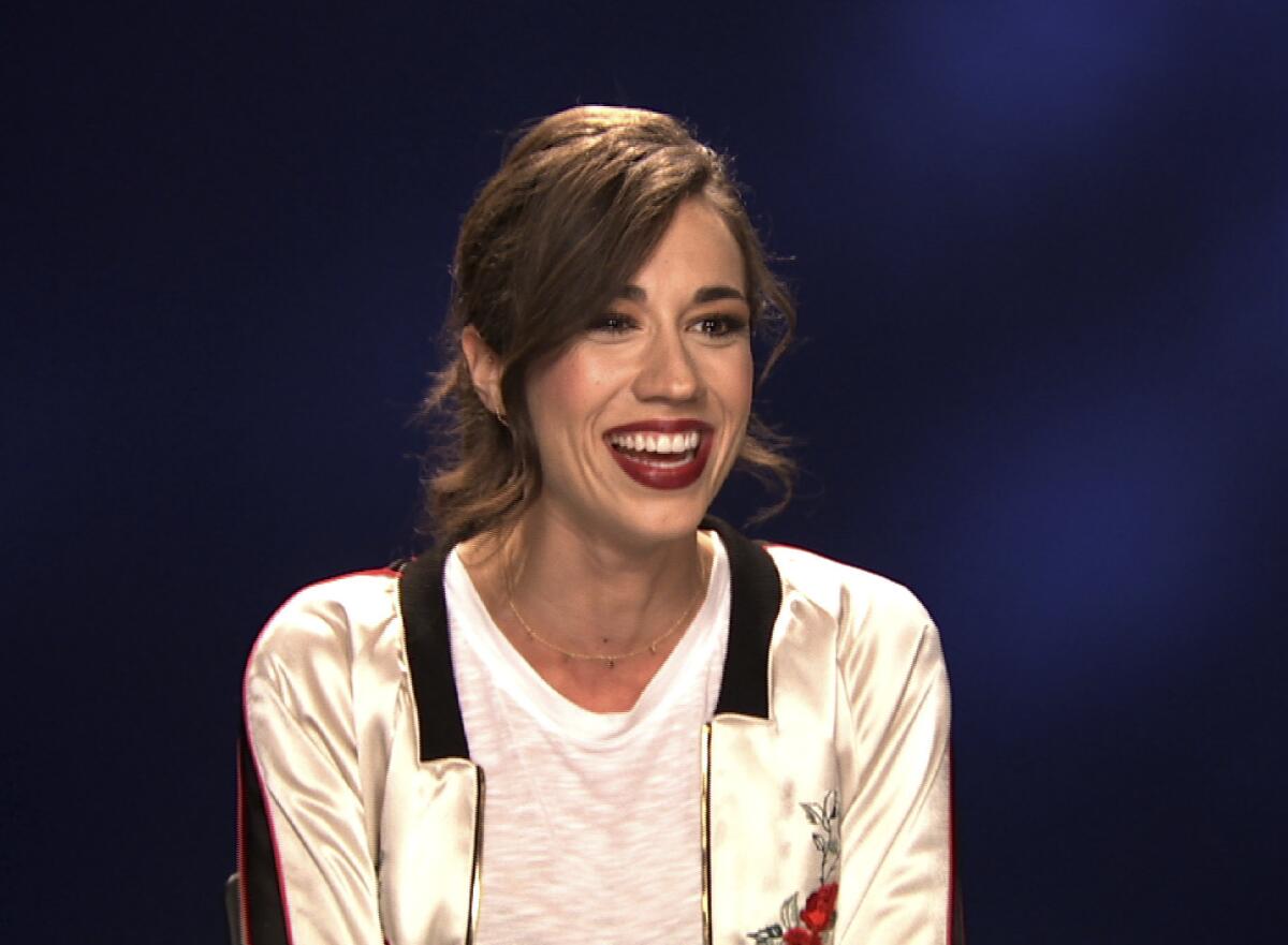 Colleen Ballinger smiles, wearing a beige jacket and white shirt with her hair up and bangs to the side.