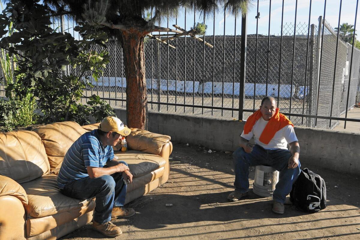 Javier Segovia, left, and Hernando Pena sit next to a giant city-owned pile of asphalt next to the Home Depot on Balboa Place in Van Nuys. Residents of the area complain about dust swirling off the pile.
