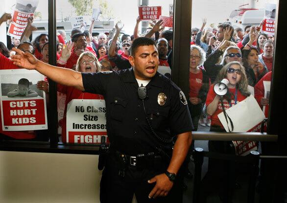 An officer keeps order inside the LAUSD building while a loud crowd of teachers and supporters rallies outside.
