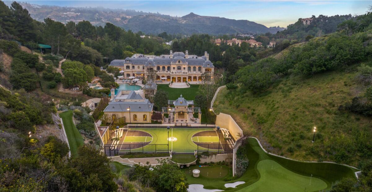 Aerial view of European-inspired mansion, basketball court, golf course and landscaped grounds surrounded by hills.