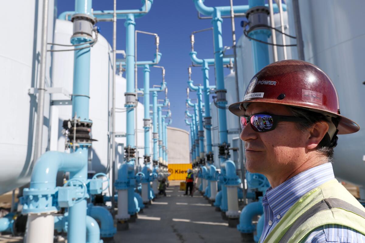 A man in a hard hat near a collection of filtration tanks outdoors.