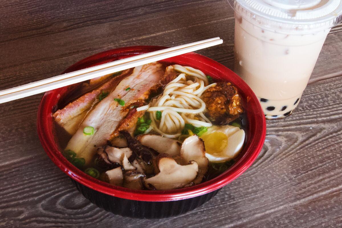 A red bowl of pork ramen with nori, corn, egg and green onion, next to a cup of boba milk tea