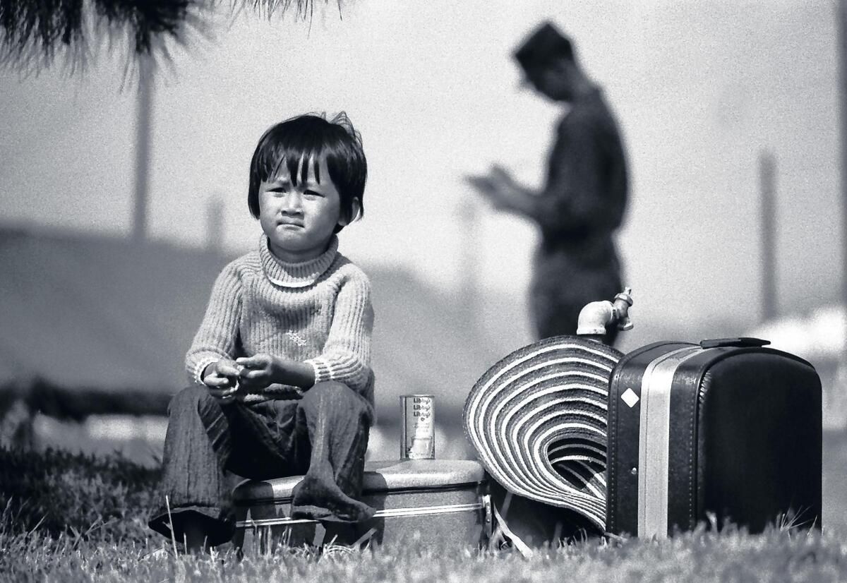 A young Vietnamese boy sits on a suitcase while his family is being processed into the Camp Talega refugee center at Camp Pendleton in 1975.