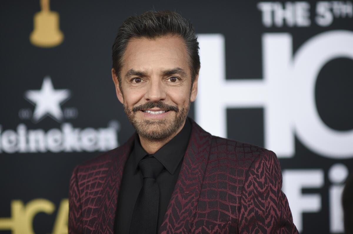 A man with a mustache smiling in a patterned black-and-maroon suit