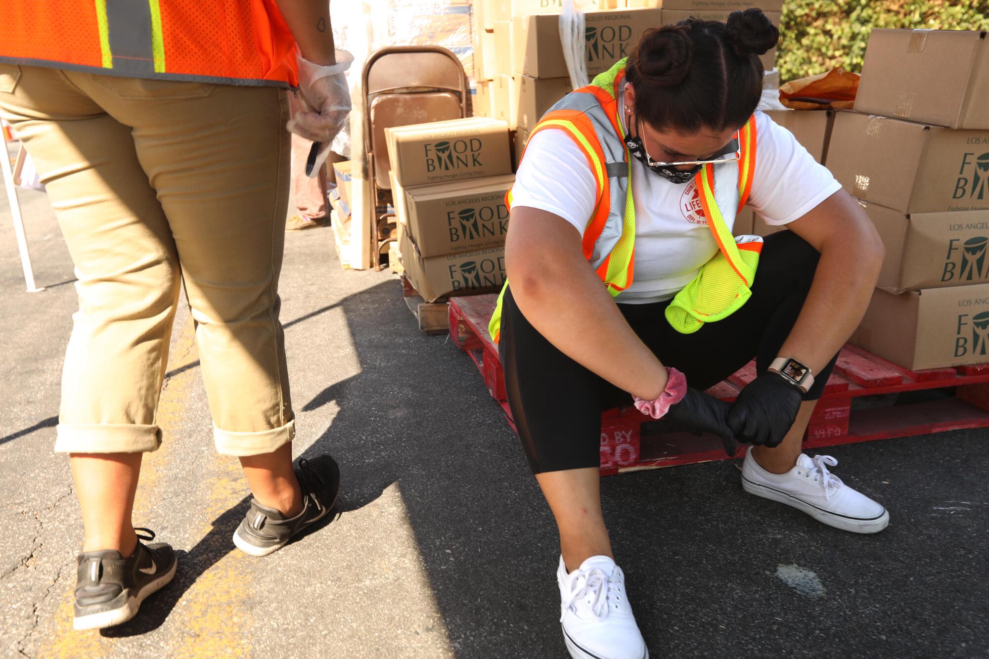 A woman in a high-vis vest sits on a wooden pallet next to cardboard boxes