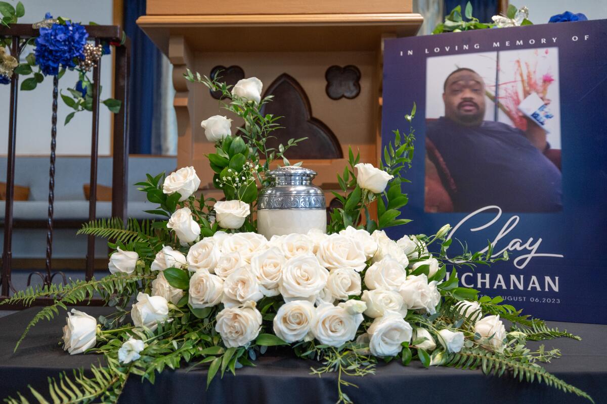 An urn is surrounded by an arrangement of white roses. Behind the flowers stands a photo of a man.